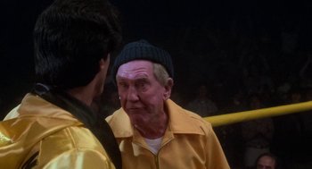 Movie still from “Rocky III” (1982), directed by Sylvester Stallone – An older man wearing a yellow jacket and a black hat; Close Up shot, Over the shoulder angle