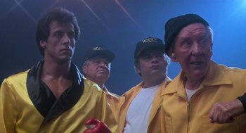 Movie still from “Rocky III” (1982), directed by Sylvester Stallone – A group of people wearing yellow jackets and hats; Medium shot, Low angle