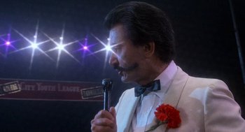 Movie still from “Rocky III” (1982), directed by Sylvester Stallone – A man in a white suit holding a microphone; Close Up shot, Low angle