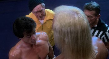 Movie still from “Rocky III” (1982), directed by Sylvester Stallone – A man is talking to two other people; Medium shot, Over the shoulder angle