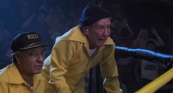 Movie still from “Rocky III” (1982), directed by Sylvester Stallone – An older man in a yellow raincoat and a hat; Medium shot, Low angle