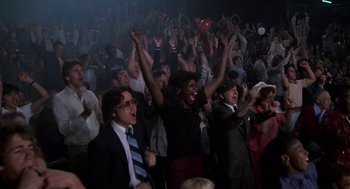 Movie still from “Rocky III” (1982), directed by Sylvester Stallone – A group of people in a room with their hands in the air; Wide shot, High angle