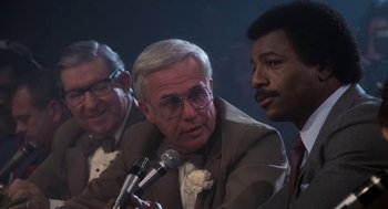 Movie still from “Rocky III” (1982), directed by Sylvester Stallone – A group of men sitting next to each other holding microphones; Close Up shot, Low angle