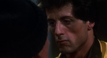 Movie still from “Rocky III” (1982), directed by Sylvester Stallone – A man's face in a dark room; Close Up shot, Over the shoulder angle