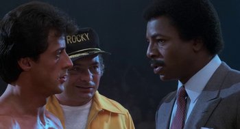 Movie still from “Rocky III” (1982), directed by Sylvester Stallone – A group of men standing next to each other in a room; Close Up shot, Low angle