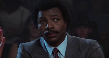 Movie still from “Rocky III” (1982), directed by Sylvester Stallone – A man in a suit and tie looking at the camera; Close Up shot, Low angle