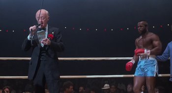 Movie still from “Rocky III” (1982), directed by Sylvester Stallone – An older man in a suit and tie standing in a boxing ring; Medium shot, Over the shoulder angle