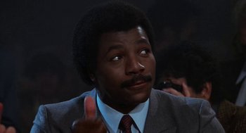 Movie still from “Rocky III” (1982), directed by Sylvester Stallone – A man in a suit and tie giving the middle finger; Close Up shot, Low angle