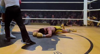 Movie still from “Rocky III” (1982), directed by Sylvester Stallone – A man laying on the ground in a boxing ring; Wide shot, High angle
