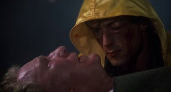 Movie still from “Rocky III” (1982), directed by Sylvester Stallone – A man in a yellow raincoat with a knife in his mouth; Close Up shot, Low angle