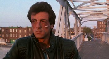 Movie still from “Rocky III” (1982), directed by Sylvester Stallone – A man with a cigarette in his mouth and wearing a leather jacket; Close Up shot, Low angle