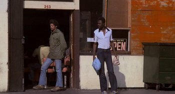 Movie still from “Rocky III” (1982), directed by Sylvester Stallone – Two men walking on the sidewalk in front of a building; Wide shot, Low angle