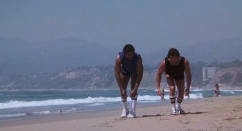 Movie still from “Rocky III” (1982), directed by Sylvester Stallone – A group of people standing on top of a sandy beach; Wide shot, Low angle