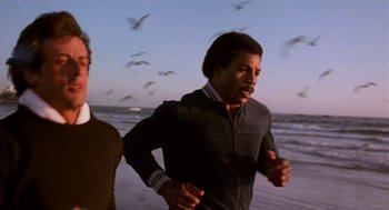 Movie still from “Rocky III” (1982), directed by Sylvester Stallone – Two men running on the beach at sunset; Medium shot, Low angle