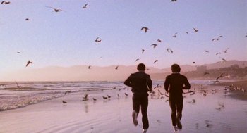 Movie still from “Rocky III” (1982), directed by Sylvester Stallone – Two people running on the beach near the ocean; Wide shot, Low angle