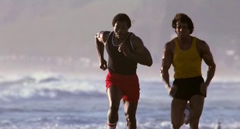 Movie still from “Rocky III” (1982), directed by Sylvester Stallone – Two men running along the beach near the ocean; Medium shot, Low angle