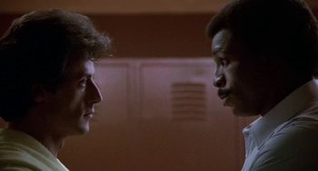 Movie still from “Rocky III” (1982), directed by Sylvester Stallone – Two men face each other in a room; Close Up shot, Low angle