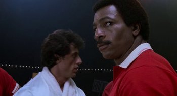 Movie still from “Rocky III” (1982), directed by Sylvester Stallone – Two men standing next to each other in front of a black background; Close Up shot, Low angle