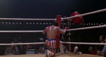 Movie still from “Rocky III” (1982), directed by Sylvester Stallone – A man kneeling down in a boxing ring; Wide shot, Low angle