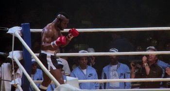Movie still from “Rocky III” (1982), directed by Sylvester Stallone – A man in a boxing ring wearing red gloves; Wide shot, Low angle