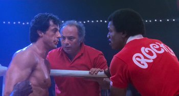 Movie still from “Rocky III” (1982), directed by Sylvester Stallone – A group of men standing next to each other in a boxing ring; Medium shot, Over the shoulder angle