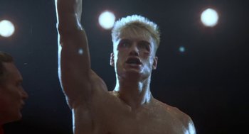 Movie still from “Rocky V” (1990), directed by John G. Avildsen – A shirtless man with blond hair is holding his arm up; Close Up shot, Low angle