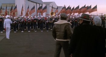 Movie still from “Rocky V” (1990), directed by John G. Avildsen – A group of men standing in front of a marching band; Wide shot, High angle