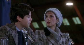 Movie still from “Rocky V” (1990), directed by John G. Avildsen – A woman and a young boy are standing next to each other; Close Up shot, Over the shoulder angle