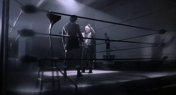 Movie still from “Rocky V” (1990), directed by John G. Avildsen – Two men in a boxing ring with a woman in the background; Wide shot, Low angle