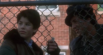 Movie still from “Rocky V” (1990), directed by John G. Avildsen – Two people standing next to each other in front of a chain link fence; Medium shot, Over the shoulder angle