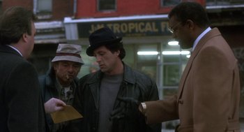 Movie still from “Rocky V” (1990), directed by John G. Avildsen – A group of men standing next to each other on a street; Medium shot, Over the shoulder angle