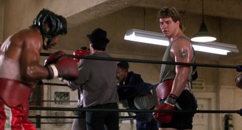 Movie still from “Rocky V” (1990), directed by John G. Avildsen – A group of people in a boxing ring with gloves on; Medium shot, Low angle