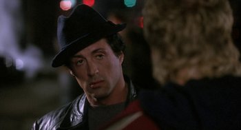 Movie still from “Rocky V” (1990), directed by John G. Avildsen – A man in a black hat and a leather jacket; Close Up shot, Over the shoulder angle
