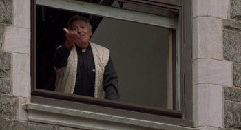 Movie still from “Rocky V” (1990), directed by John G. Avildsen – An older man wearing a priest's outfit is looking out of a window; Medium shot, Low angle