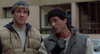 Movie still from “Rocky V” (1990), directed by John G. Avildsen – A man and a boy standing next to each other on the sidewalk; Close Up shot, Low angle