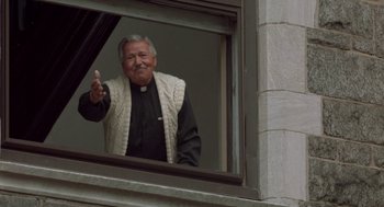 Movie still from “Rocky V” (1990), directed by John G. Avildsen – An older man wearing a white sweater is looking out of a window; Medium shot, Low angle