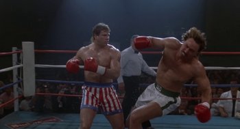 Movie still from “Rocky V” (1990), directed by John G. Avildsen – Two men in red and white boxing gloves in a boxing ring; Medium shot, Low angle
