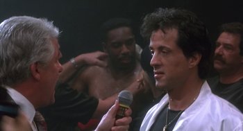 Movie still from “Rocky V” (1990), directed by John G. Avildsen – A man is being interviewed by a reporter in front of another man; Close Up shot, Over the shoulder angle