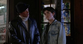 Movie still from “Rocky V” (1990), directed by John G. Avildsen – A man standing next to a young man in front of a window; Close Up shot, Over the shoulder angle