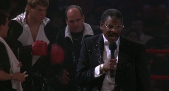 Movie still from “Rocky V” (1990), directed by John G. Avildsen – A man wearing a suit and tie holding a microphone; Medium shot, Low angle