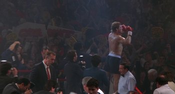 Movie still from “Rocky V” (1990), directed by John G. Avildsen – A man in a boxing ring with people in the background; Wide shot, Low angle