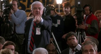 Movie still from “Rocky V” (1990), directed by John G. Avildsen – A man in a suit and tie waving at a crowd; Medium shot, Over the shoulder angle