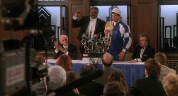 Movie still from “Rocky V” (1990), directed by John G. Avildsen – Two men standing in front of microphones at a press conference; Wide shot, Over the shoulder angle