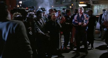 Movie still from “Rocky V” (1990), directed by John G. Avildsen – A group of people standing on the sidewalk at night; Wide shot, Over the shoulder angle