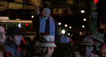 Movie still from “Rocky V” (1990), directed by John G. Avildsen – An older man wearing a hat and wearing a priest's outfit; Medium shot, Low angle