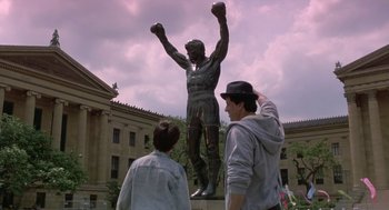 Movie still from “Rocky V” (1990), directed by John G. Avildsen – A statue of a man with a boxing glove on his head; Wide shot, Low angle