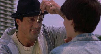 Movie still from “Rocky V” (1990), directed by John G. Avildsen – A man is putting a hat on a boy's head; Close Up shot, Over the shoulder angle