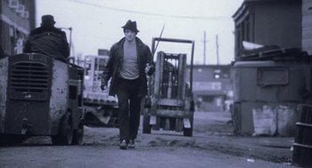 Movie still from “Rocky V” (1990), directed by John G. Avildsen – A man walking down a street holding a stick; Wide shot, Low angle
