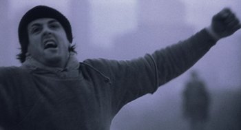 Movie still from “Rocky V” (1990), directed by John G. Avildsen – A man in a gray jacket is holding his arm up; Close Up shot, Low angle