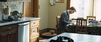 Movie still from “Salt” (2010), directed by Phillip Noyce – A man sitting at a table with a dog in a room; Wide shot, Over the shoulder angle